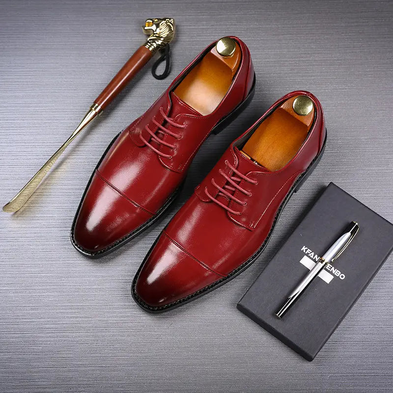 Herren-Businessschuhe im britischen Stil mit spitz zulaufender Zehenpartie aus Kunstleder, poliertes Rot mit Kappenzehen-Design, passenden Schnürsenkeln und zusammen mit goldfarbenen Schuhspannerdummys präsentiert.