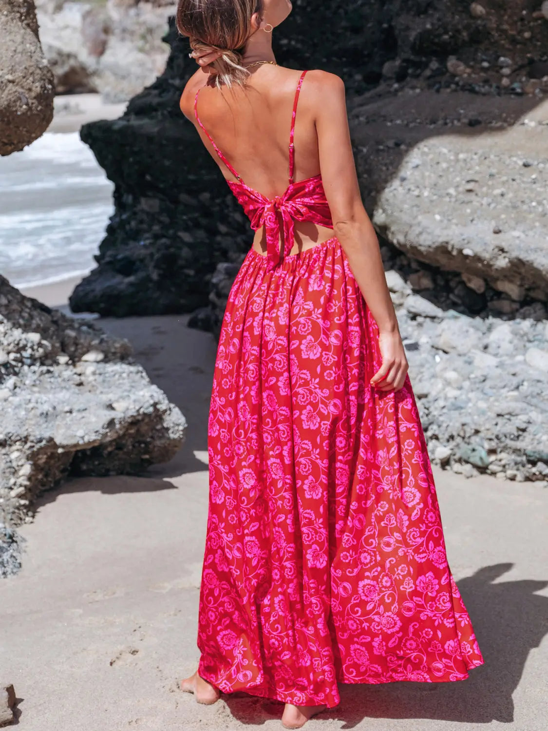 A vibrant red floral knotted v neck maxi dress with thin spaghetti straps and a back tie detail shown from the back side.