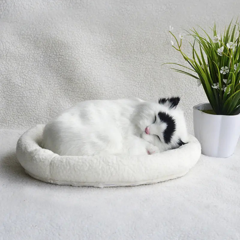 A plush white and black realistic breathing cat figurine sleeping peacefully in a soft round pet bed.