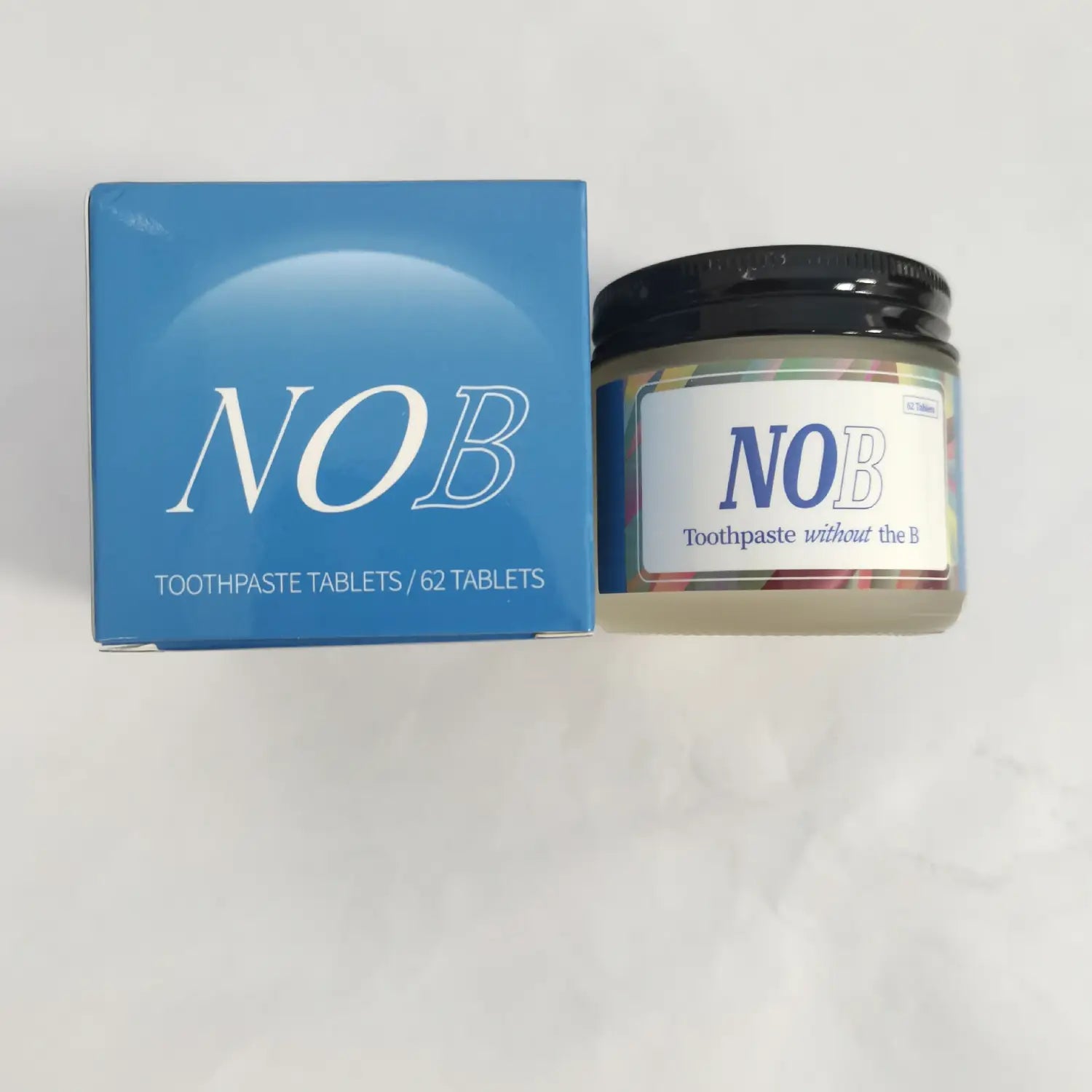 Blue rectangular box labeled nob toothpaste tablets with 62 tablets next to a clear jar with a black lid containing solid toothpaste tablets both featuring the brand name nob in white lettering used as a portable breath mint.