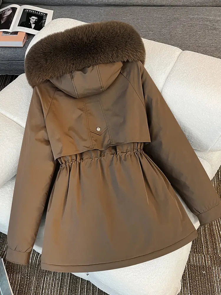 Manteau d’hiver marron à capuche, col en fourrure marron foncé duveteuse et taille resserrée, dans le style d’une parka matelassée à capuche avec col de fourrure.