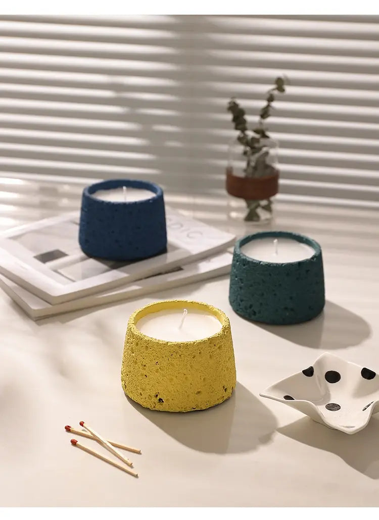 Trois supports de bougie en ciment à effet moucheté, colorés, en bleu, sarcelle et jaune, conçus comme des coupelles d’aromathérapie en ciment texturé