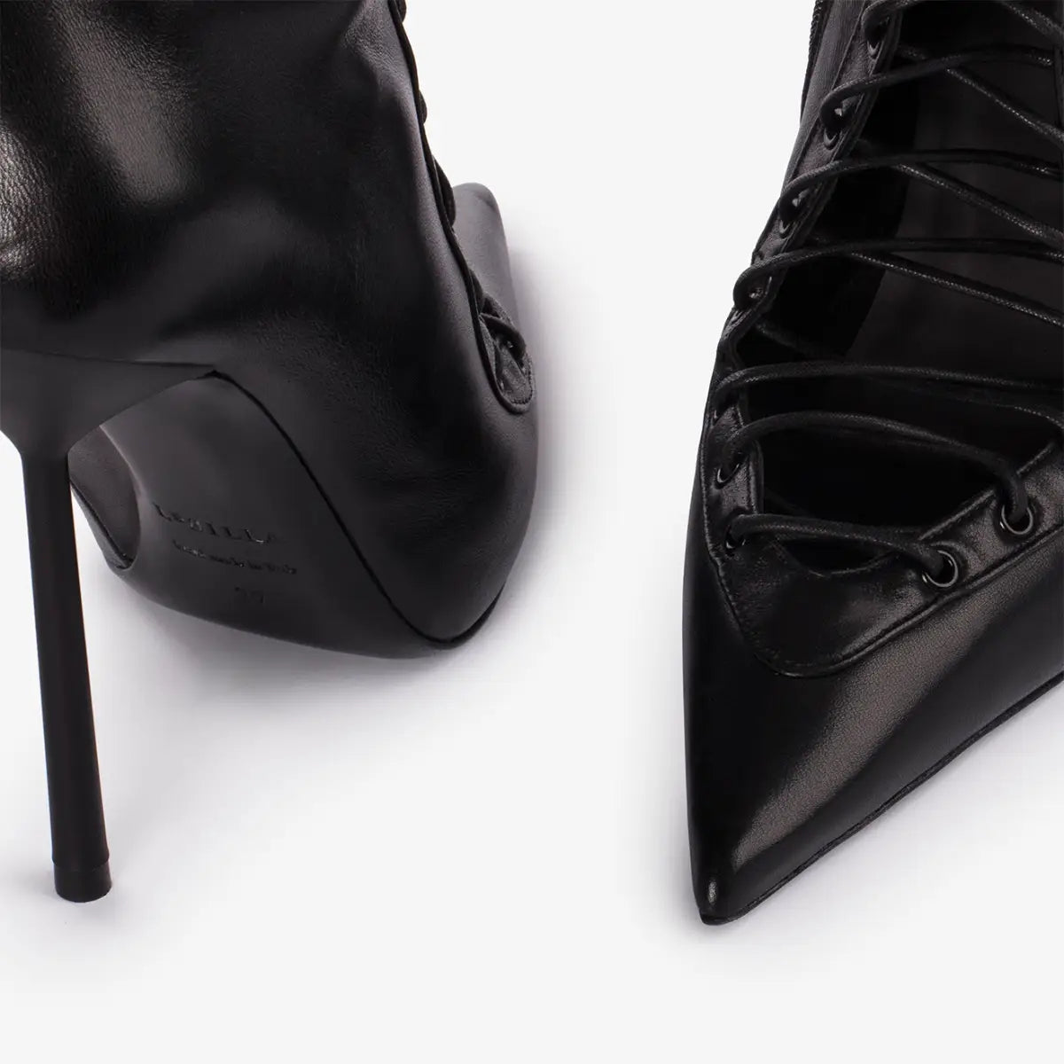 Des bottines en cuir noir à lacets, à bout pointu affirmé et à talon haut fin, présentées dans un produit de sandales à talon aiguille haut à bout pointu en mesh à lacets.