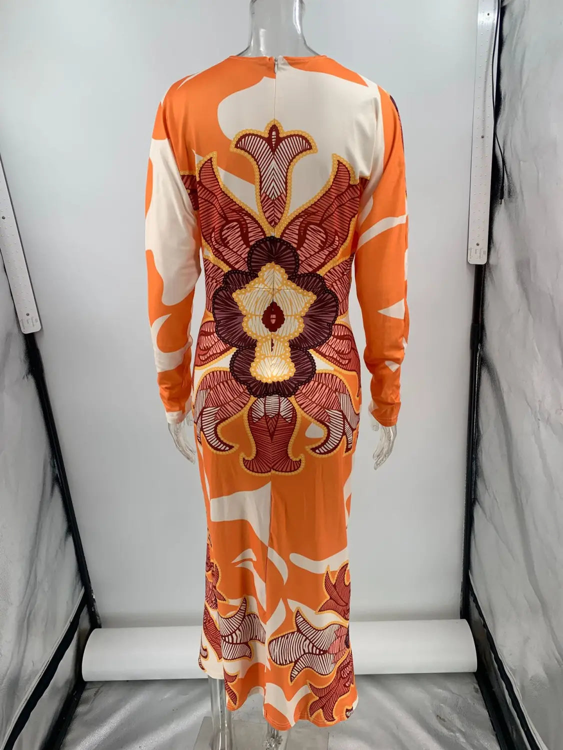 Printed v-neck geometric wrap midi dress in orange and cream with a bold symmetrical floral pattern in reds and browns and long sleeves.