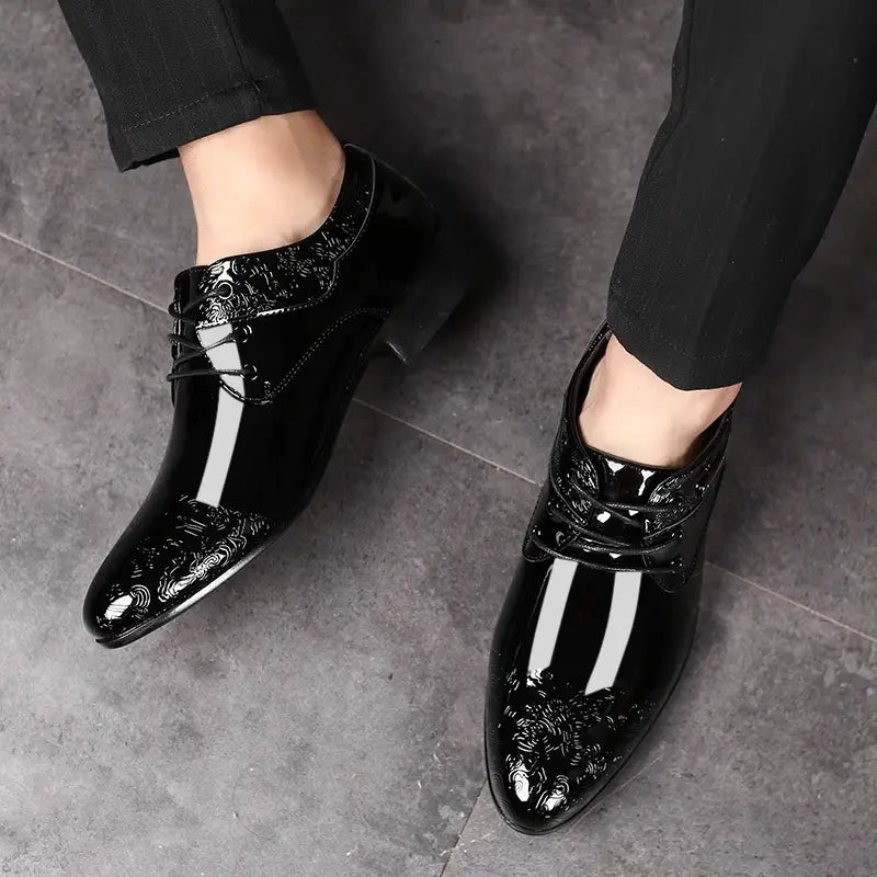 Black patent leather men’s formal business shoes with a glossy finish and intricate floral embossing along the toe cap.