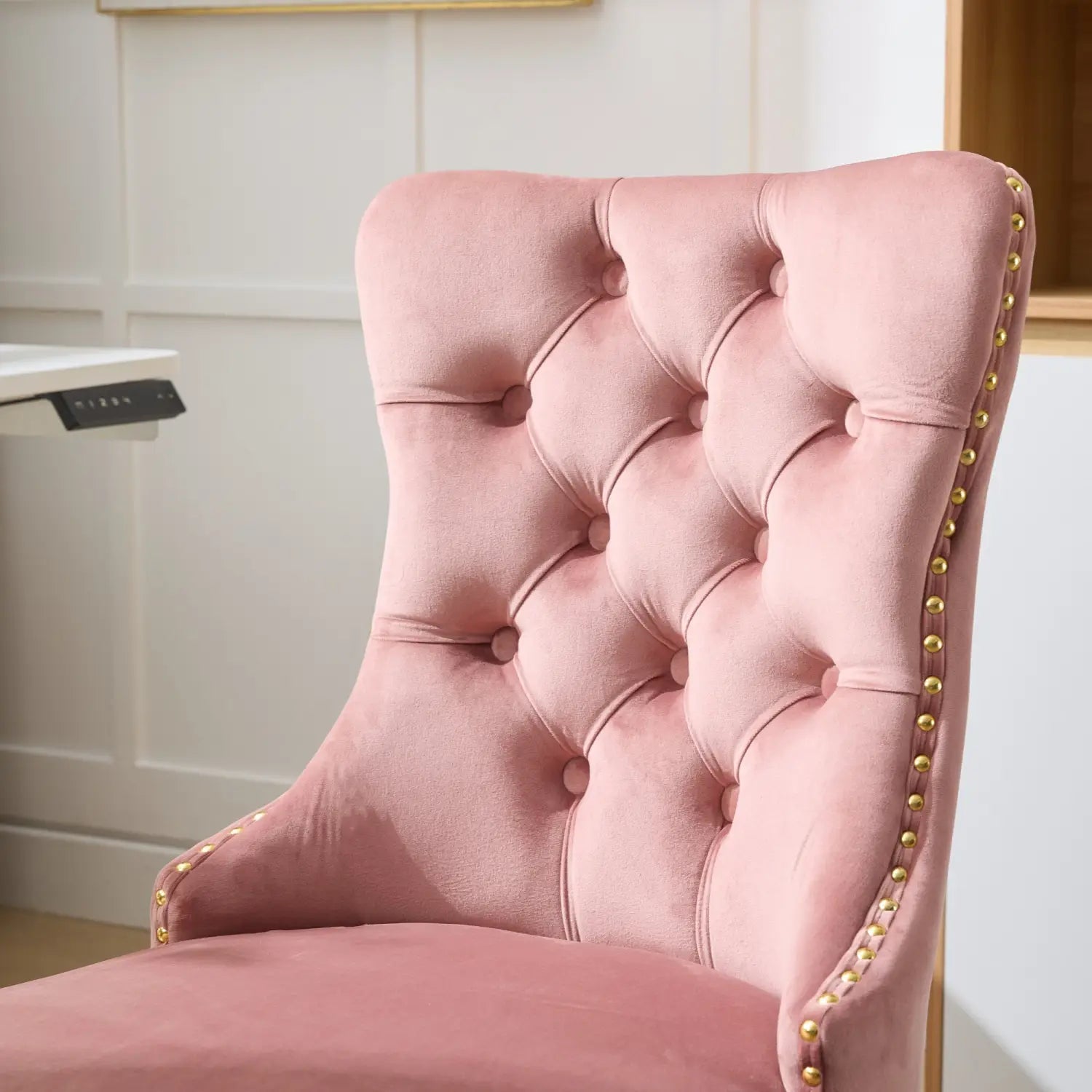 Un fauteuil de bureau moelleux en velours rose poudré, capitonné, avec une base dorée et une bordure à clous décoratifs.