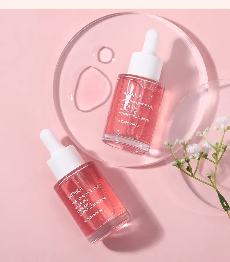 Two transparent glass dropper bottles with white caps containing pink niacinamide 10% ha 4% dark spot correcting serum from moika in 30ml size.