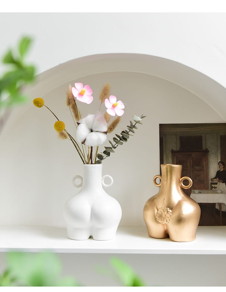 White ceramic female body ceramic vase shaped like stylized buttocks with two circular handles on the sides.