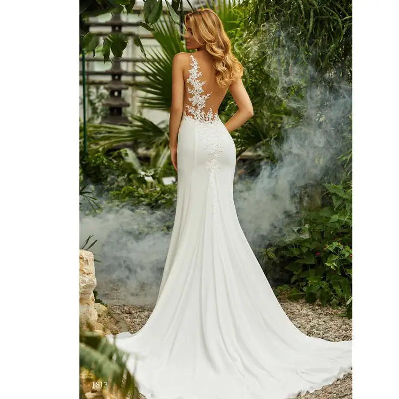A white lace mermaid wedding dress with intricate lace detailing along the back and a flowing train shown from the back side.