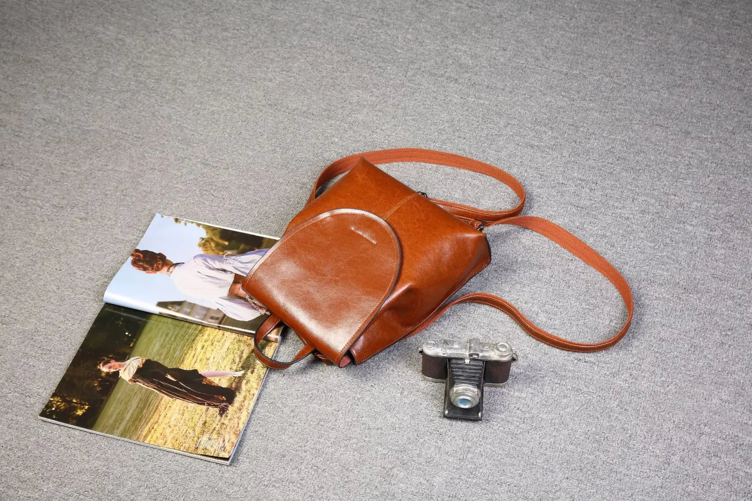 Una mochila bandolera de cuero marrón cálido con solapa superior redondeada y correas de hombro ajustables, en un diseño de moda retro.