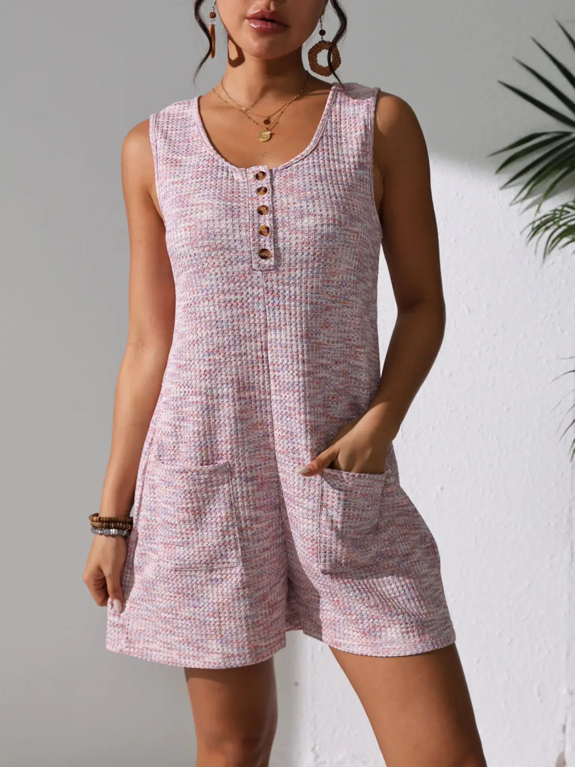 A soft pink waffle knit button front sleeveless pocket romper featuring a textured fabric and two front pockets.