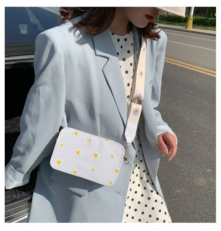 White crossbody bag with yellow and white daisy embroidery featuring a chain strap made of pu leather.