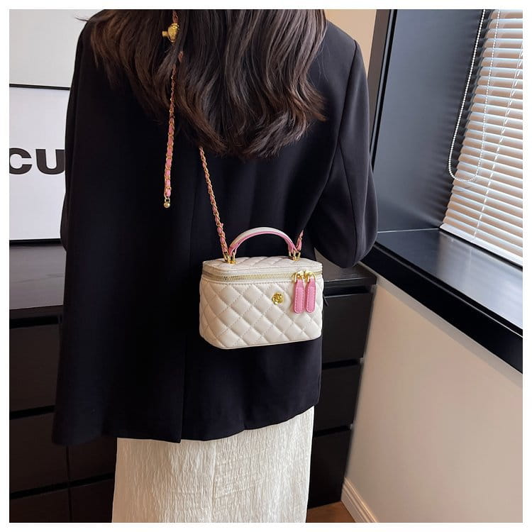 A cream-colored quilted diamond crossbody bag made of pu leather with pink handles tassels gold-tone hardware and a chain strap.