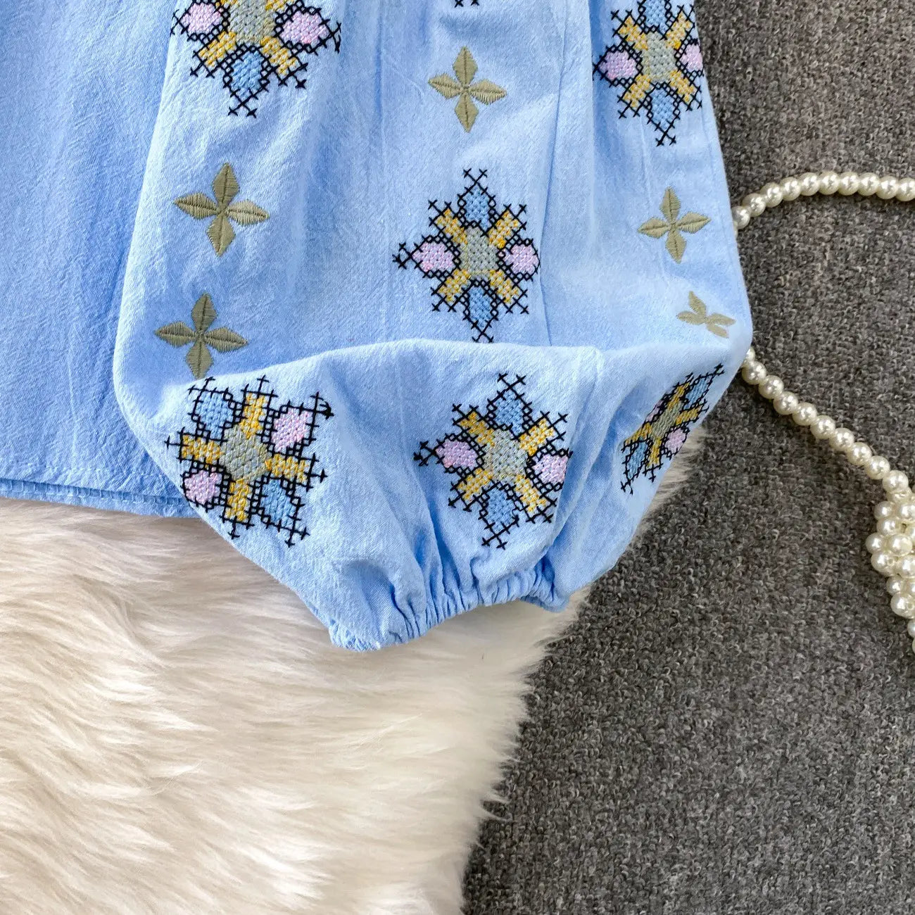 Light blue cotton embroidered lantern sleeve tie neck blouse with colorful pink yellow and beige floral cross-stitch patterns.