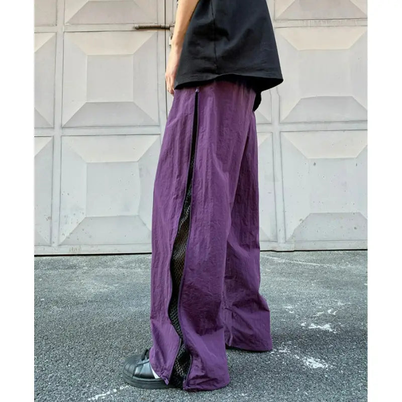 Pantalon de randonnée utilitaire à panneau latéral en mesh violet avec fermeture éclair noire sur le côté, révélant une doublure en mesh et une coupe à jambe large
