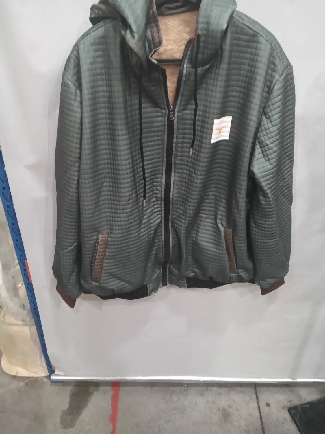 Veste à capuche zippée doublée de polaire pour homme en tissu matelassé vert foncé, fermeture éclair noire et passepoils marron sur les poches.