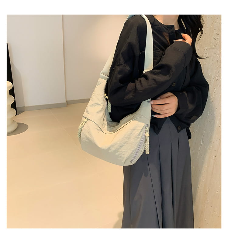 Light gray nylon crossbody bag with large capacity hobo shoulder design and braided rope detailing on the zipper pulls.