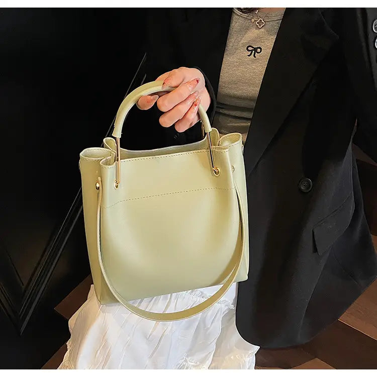Minimalist leather bucket bag in soft pale green leather with gold-tone hardware and detachable matching shoulder strap.