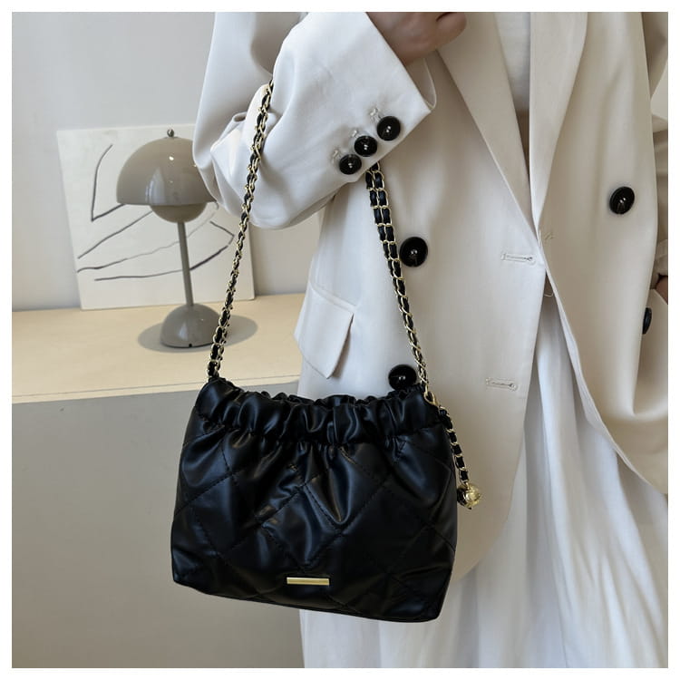 Black quilted faux leather crossbody bag with gold-tone chain strap and drawstring top closure.
