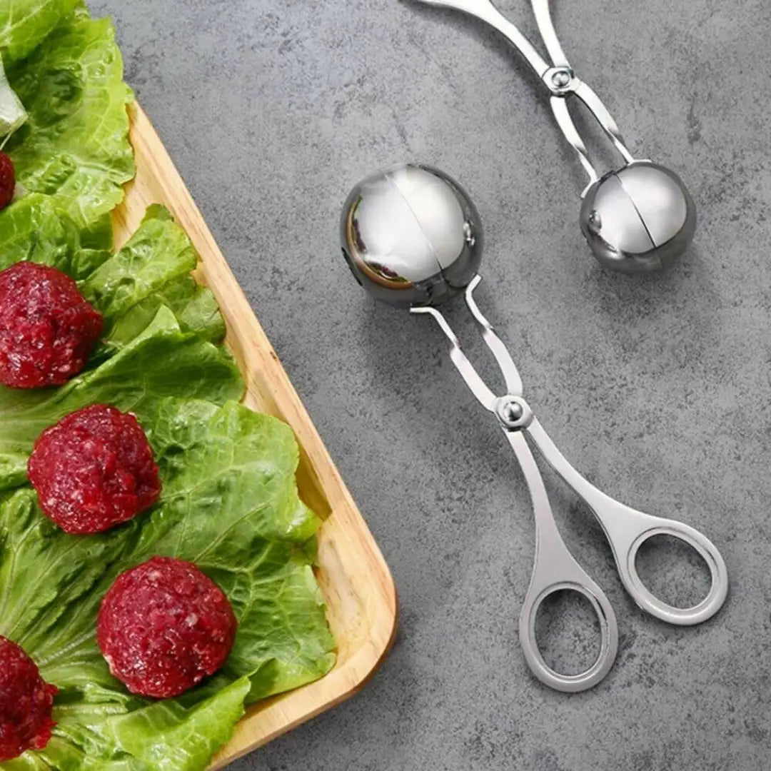 Stainless steel meatball maker tongs with shiny ball-shaped scoop and handles for serving or portioning meatballs.