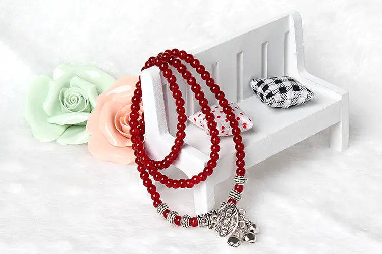 Red agate good luck bracelet featuring red beaded rosary with silver-toned metal accents and detailed elephant pendant for engraved protection charm.