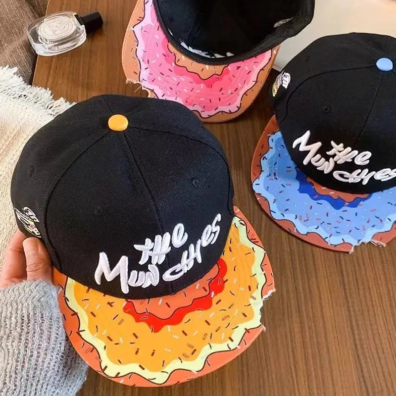 Black snapback cap with white embroidered the munchies text and colorful burger-themed flat brim featuring yellow bun red patty and brown sesame seeds, known as the munchies embroidered flat brim snapback cap.
