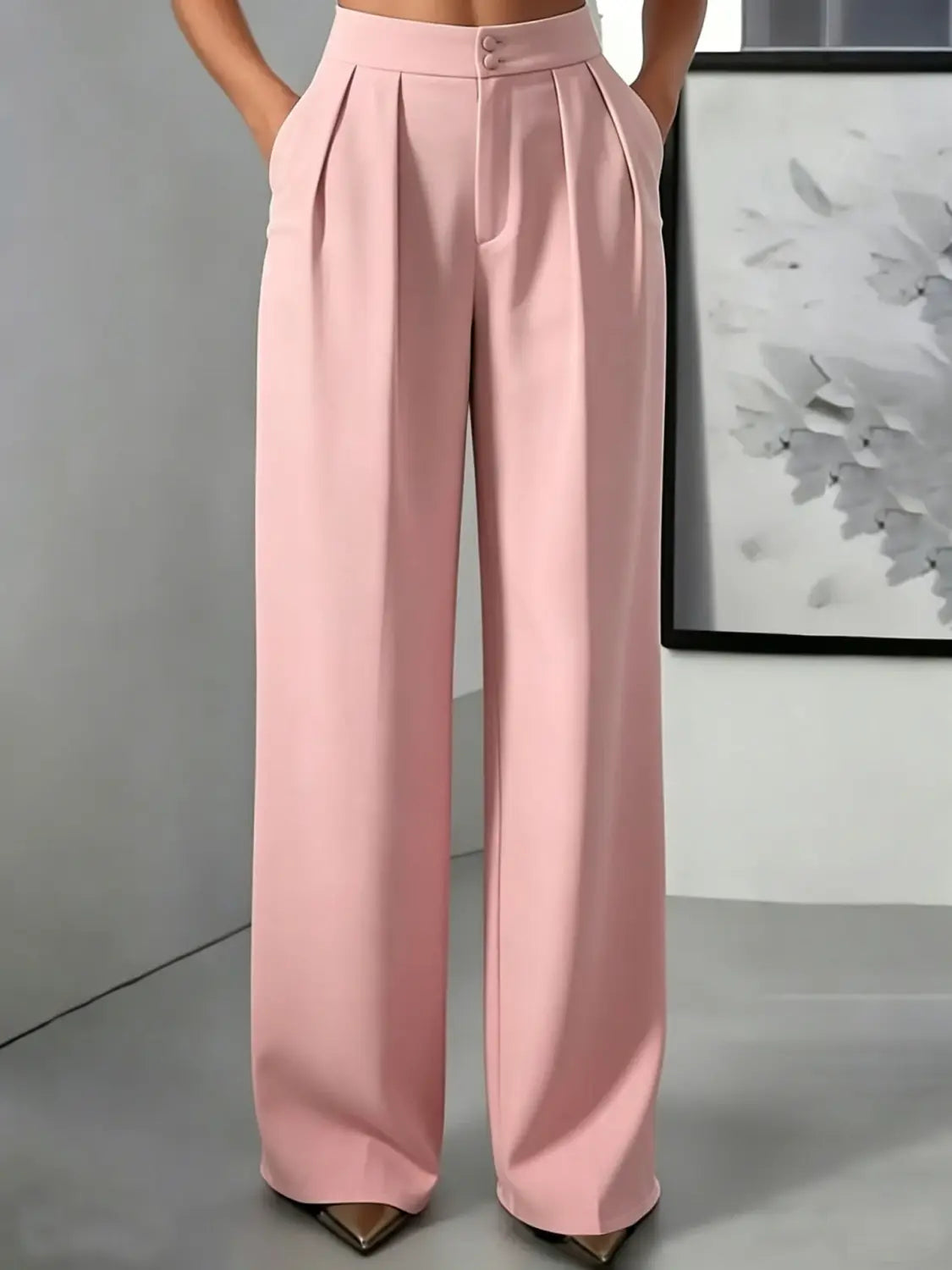 Une paire de pantalons à jambes larges et taille haute rose tendre, avec une finition élégante type satin et deux boutons à l’avant à la taille.