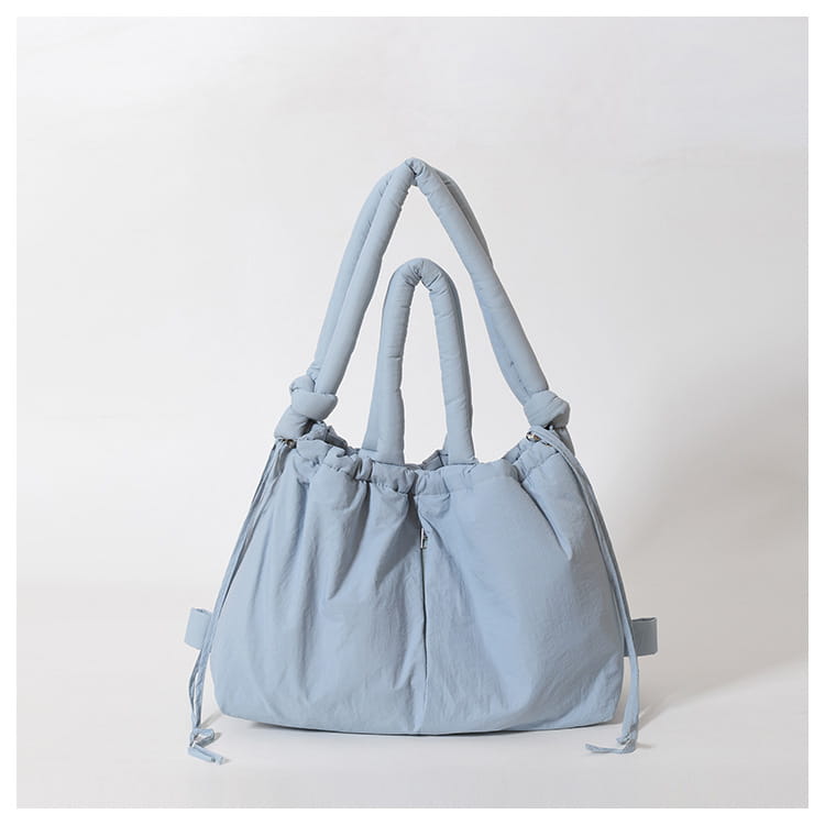 Light blue quilted puffer tote bag made of lightweight nylon with thick knotted handles and drawstring ties.