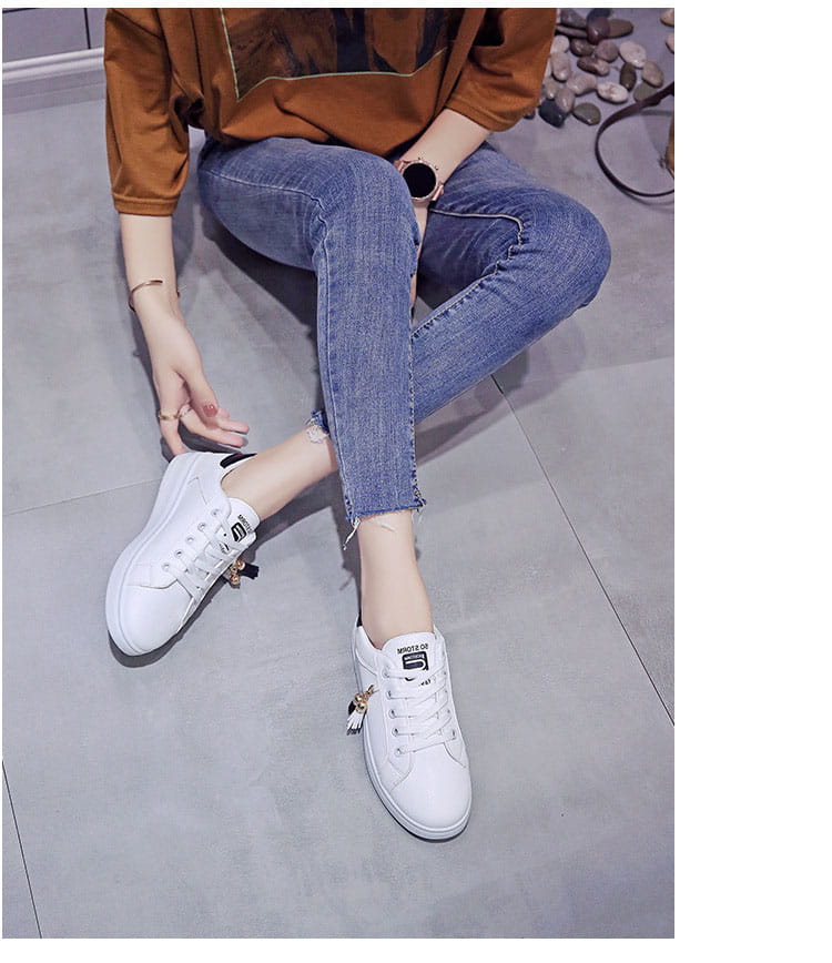 White leather platform sneakers with black branding and decorative tassels on the laces designed as breathable sports shoes.