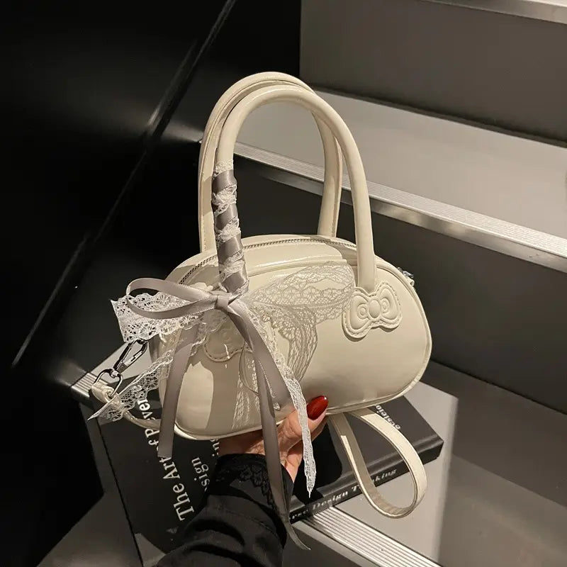 Cream-colored Hello Kitty crossbody bag with a glossy finish featuring delicate lace detailing and an embroidered bow on the front.