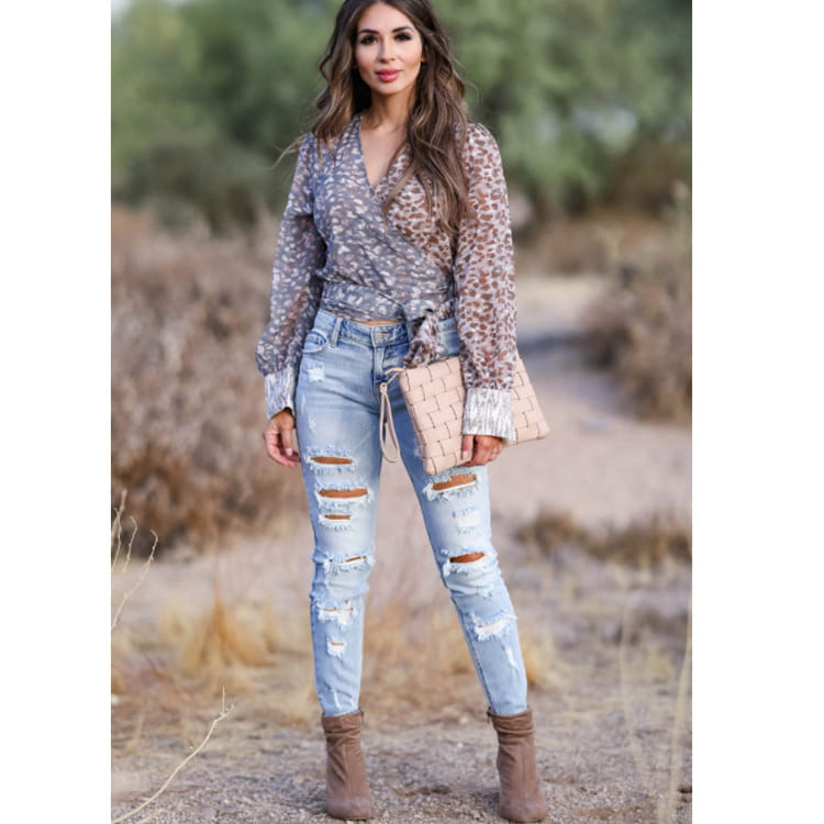 Bolso clutch tejido color beige con un patrón texturizado tipo cesta y herrajes con acabado en tono plateado, combinado con pantalones vaqueros ajustados tipo skinny desgastados con roturas