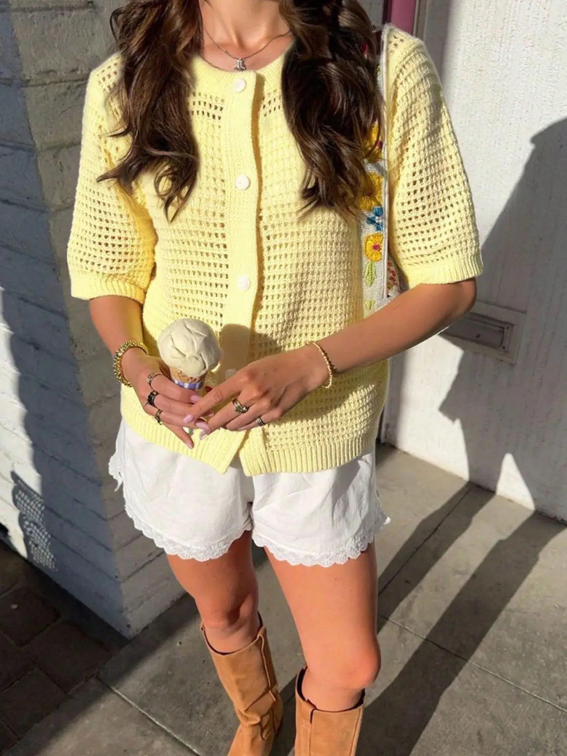 Un suéter tipo cárdigan de punto tejido al crochet amarillo suave con mangas cortas de calado y bordado floral de colores en la manga.