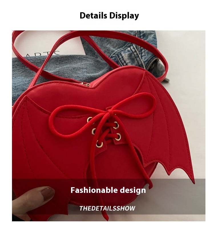 A vibrant red heart-shaped crossbody bag featuring bat-wing details and a lace-up front design.