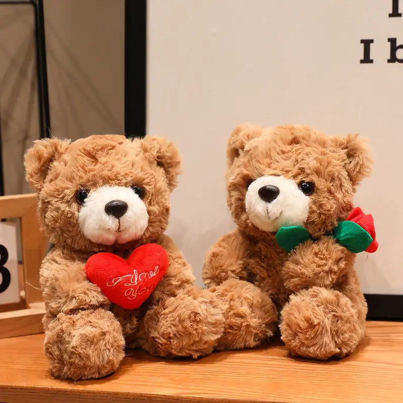 Zwei braune Plüsch-Teddybären: einer hält ein rotes, mit „I love you“ besticktes Herz und der andere trägt eine grüne Fliege mit einer kleinen roten Rose; aus der Kollektion des Teddybär-Plüschtiers mit Rosen, Valentinsgeschenk, in der Größe 16 bis 25 Zentimeter.