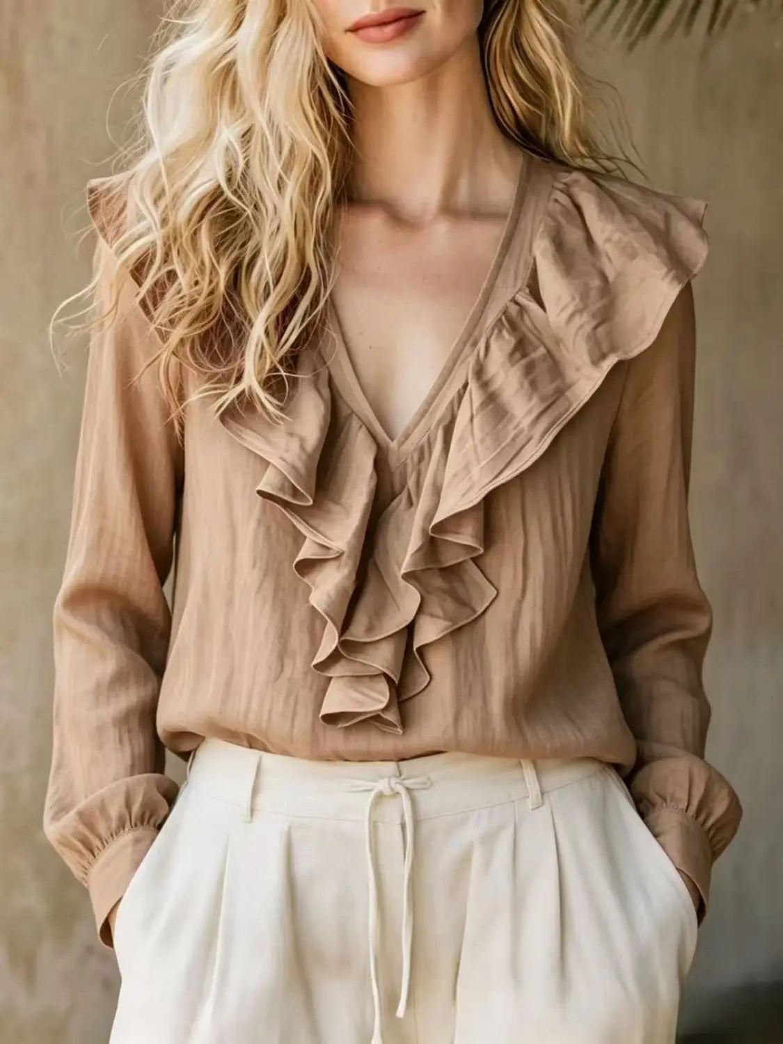 Una blusa de lino color beige suave con cuello en V y manga larga, con detalles de volantes.