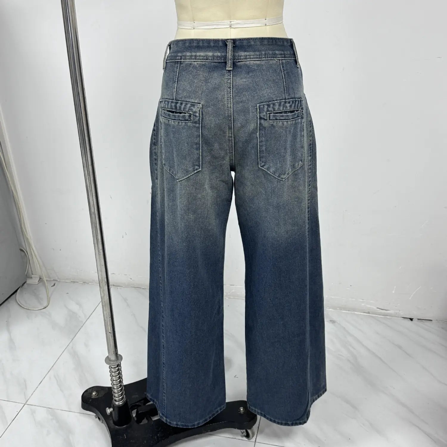 Vaqueros de mezclilla de pierna ancha de talle alto en un lavado azul descolorido, con bolsillos traseros clásicos y dobladillo recto mostrados desde el lado posterior.