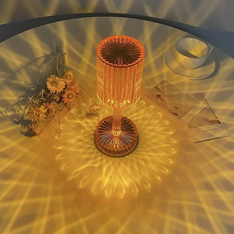 A warm amber glass crystal table lamp with a faceted cylindrical design and intricate radial patterns on its base and top featuring 3 way dimmable touch control for use as a night light.