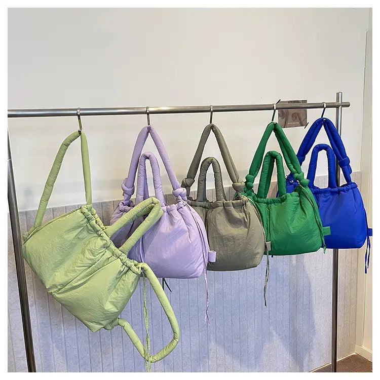 Pastel-colored quilted puffer tote bags made of lightweight nylon with drawstring closures and padded handles hanging on a metal rack.