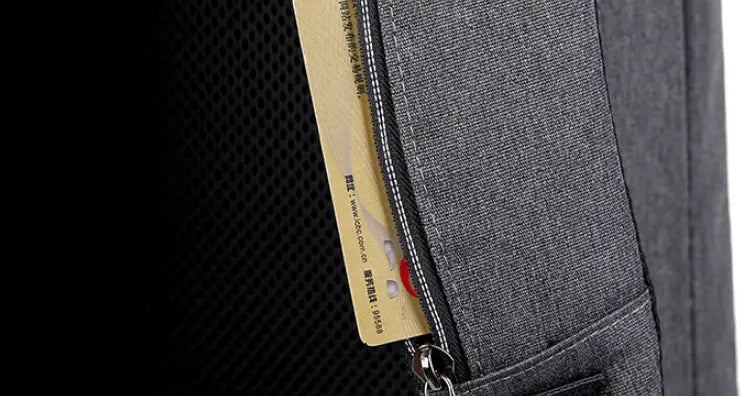 a gold-colored credit card with black text and a red logo partially visible inside the zipper of a dark gray business laptop backpack with usb charging port made of oxford cloth