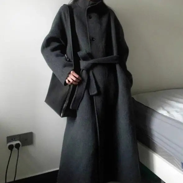 Ein langer Wollmantel in Dunkelgrau mit gegürteter Taille und knopfverdeckter Front, entworfen für kurze Größen in einem koreanischen Mid-Lenght-Stil.