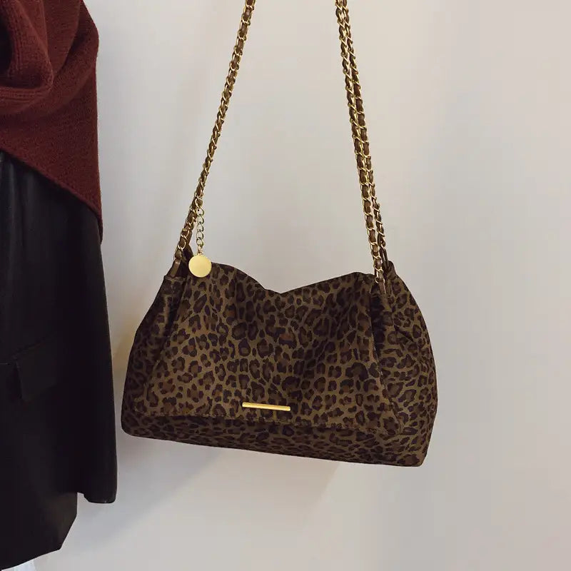 A brown leopard print crossbody bag featuring a gold chain strap and a small circular charm.