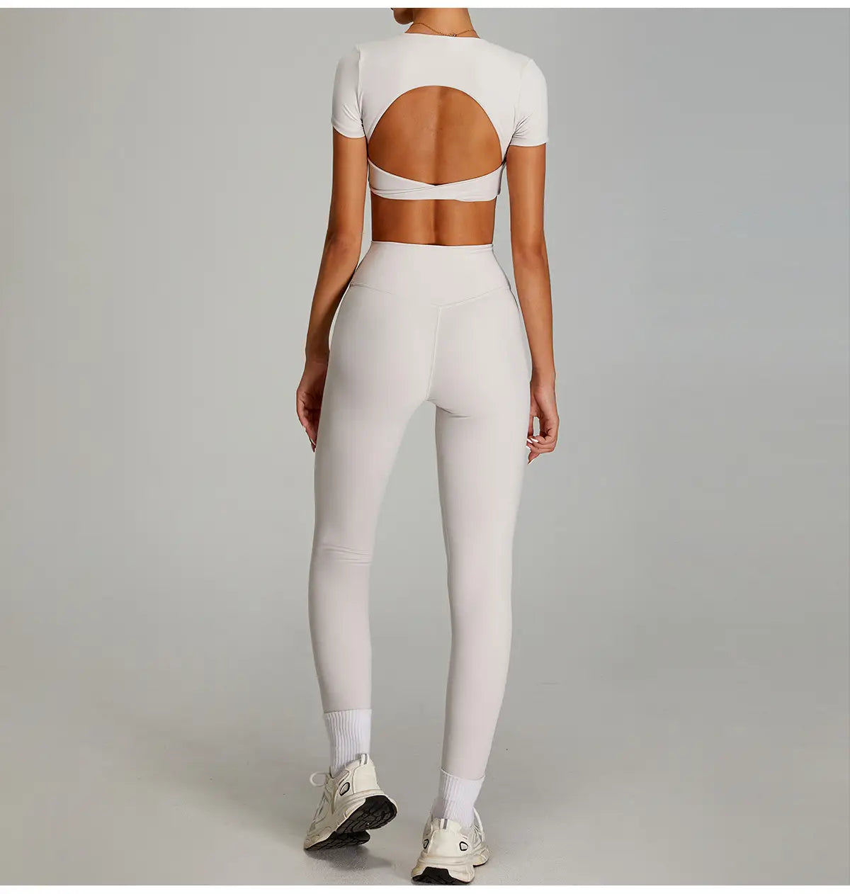 Ensemble de sport bicolore blanc cassé élégant à deux pièces, avec un haut court comportant une découpe circulaire dans le dos, et des leggings de sport à séchage rapide taille haute fabriqués dans un tissu extensible, présentés côté dos.
