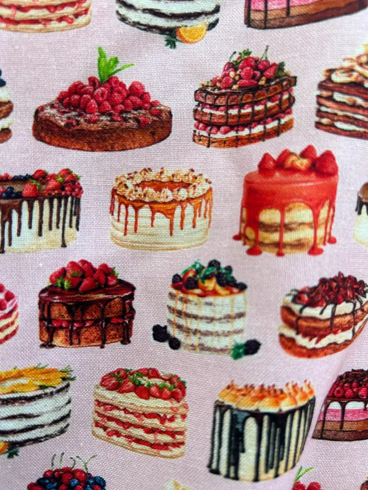 Pink pleated skater skirt featuring a repeating pattern of illustrated cakes on pink fabric