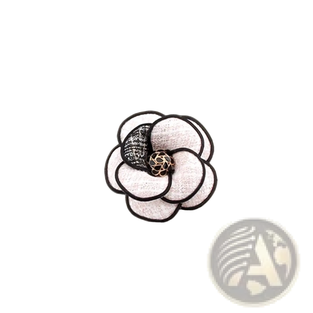 A cream-colored camellia fabric flower brooch with black embroidered edges and gold mesh center pinned to a brown coat