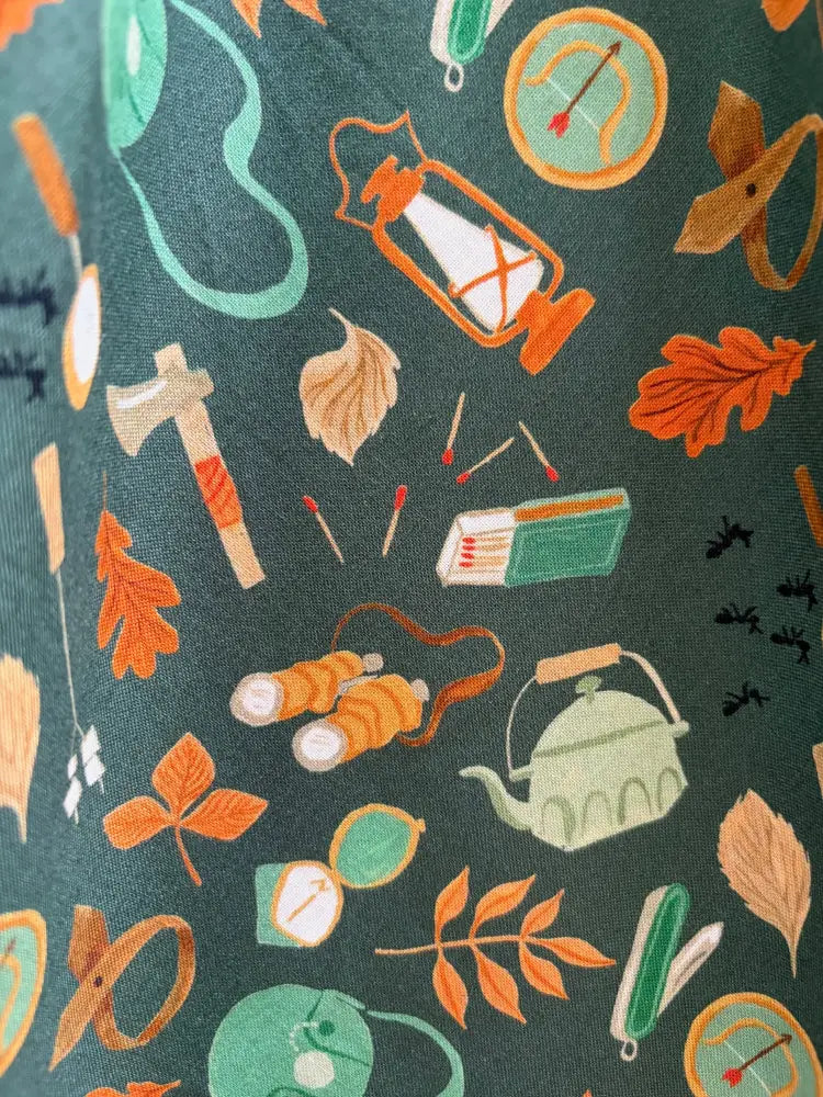 Vintage camping print cotton bow top in dark green featuring a repeating pattern of camping and outdoor gear in orange teal and beige