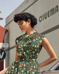 A woman wearing a vintage camping print cotton bow top in dark green with teapots, lanterns, and leaves pattern