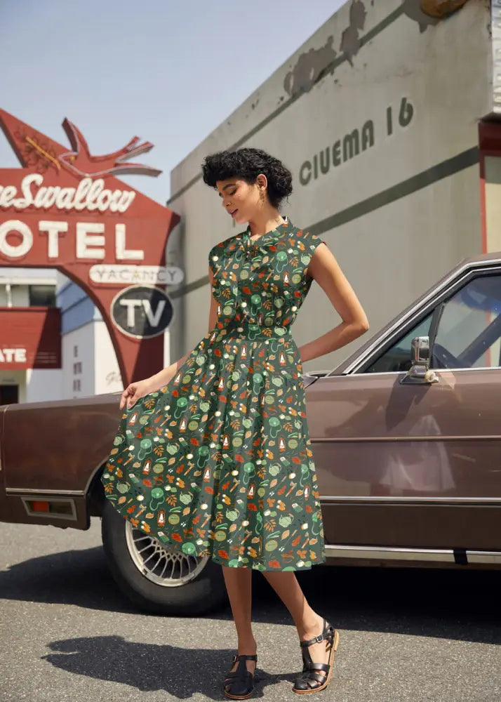 A woman wears a vintage camping print cotton bow top in dark green with a playful pattern of vegetables and herbs