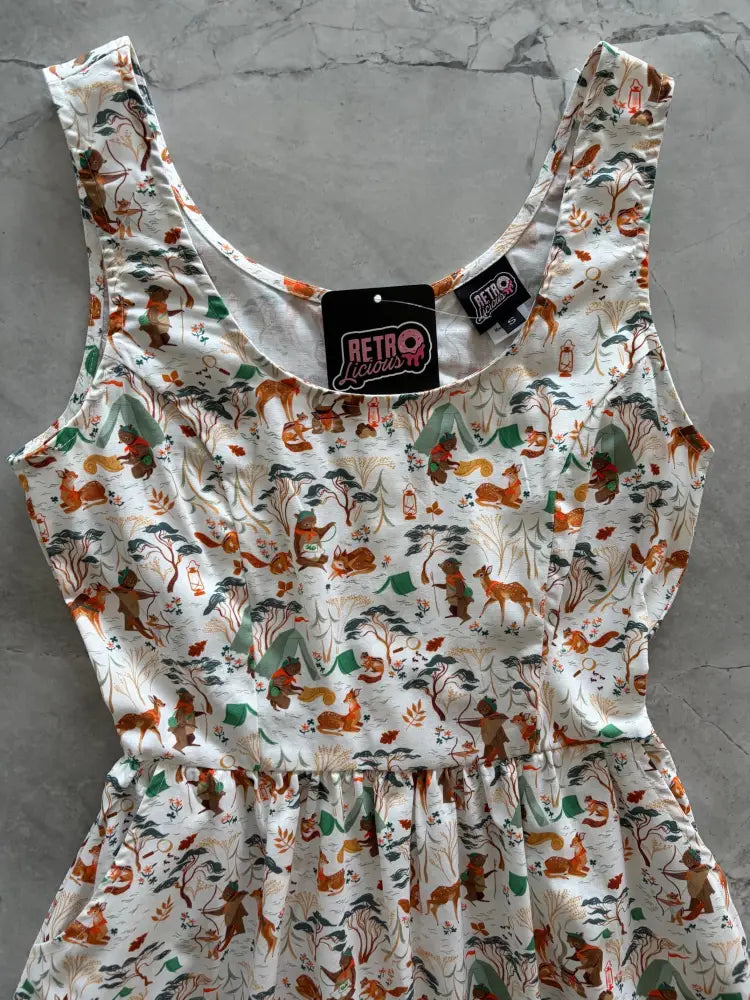 White sleeveless cotton fit and flare dress with campsite print featuring orange foxes green tents and brown trees