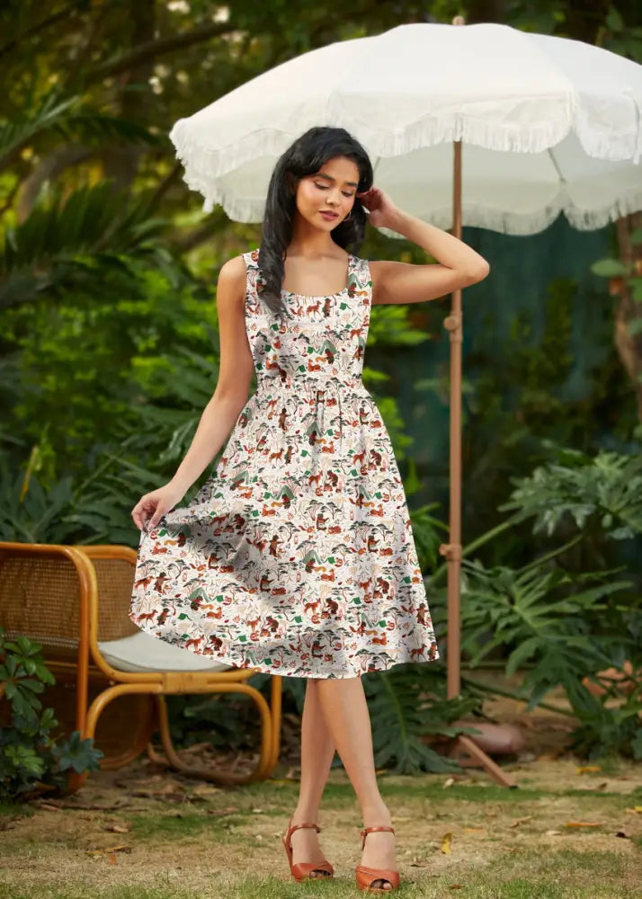 A woman wears a white sleeveless campsite print vintage fit and flare cotton dress with colorful cartoon dogs