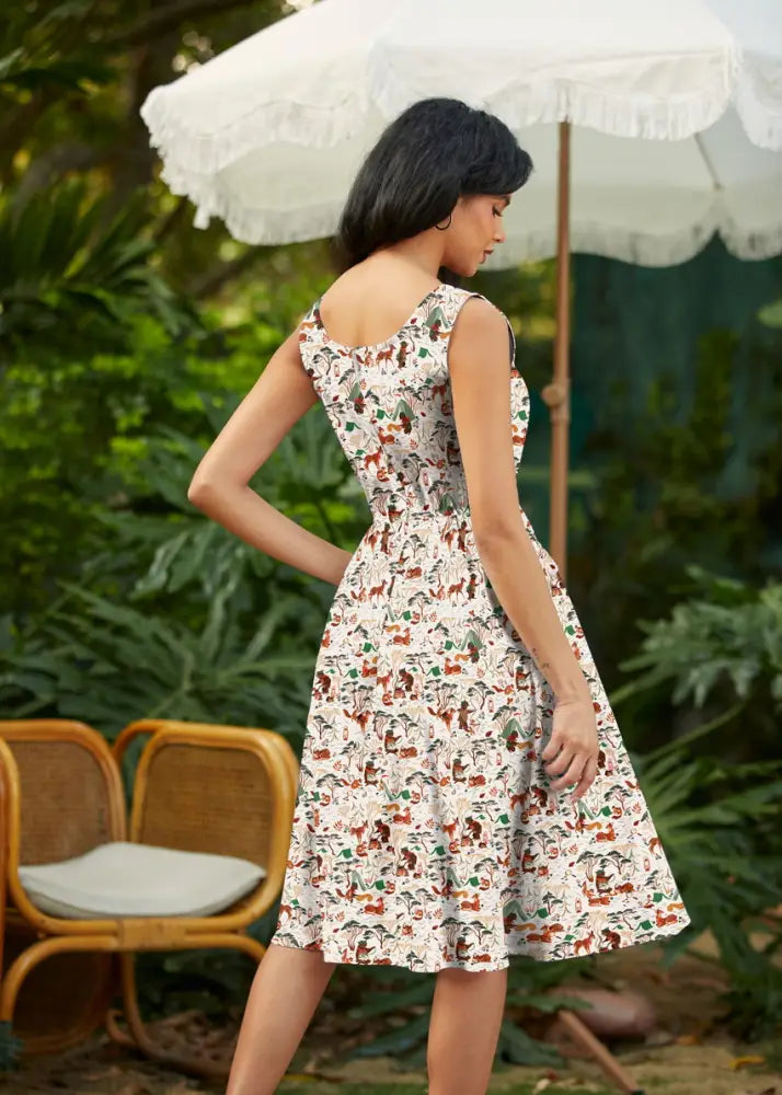 A sleeveless white vintage fit and flare cotton dress with playful campsite print of cartoon animals and foliage